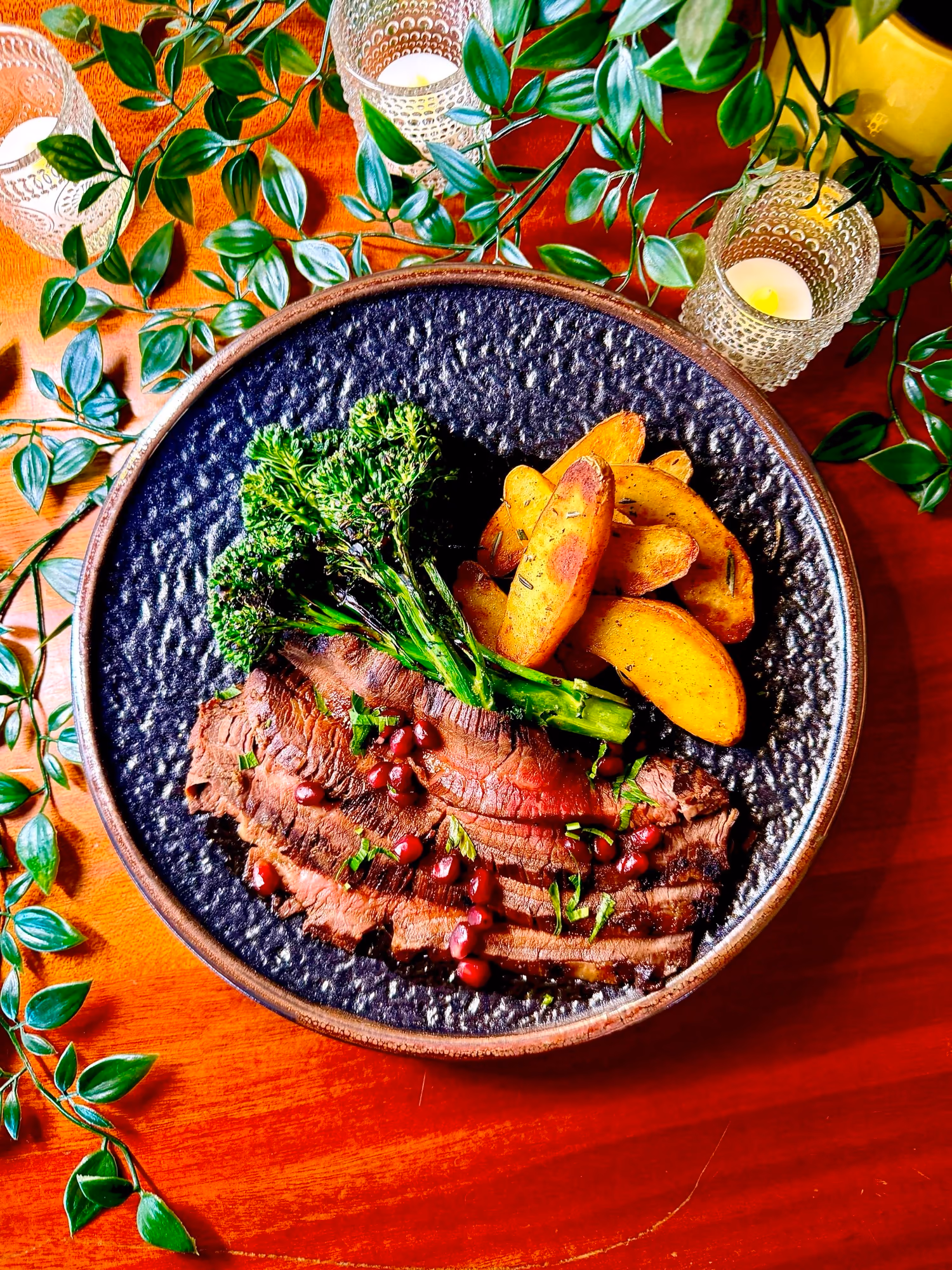 Sliced steak on a blue plate with broccolini and roasted potatoes